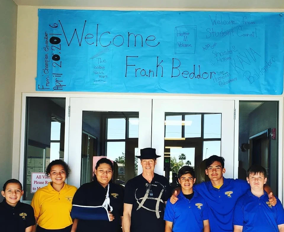 Beddor with seven students in school polo shirts at a
               school's front doors, under a long blue paper banner reading
               Welcome Frank Beddor, signed by the student council.