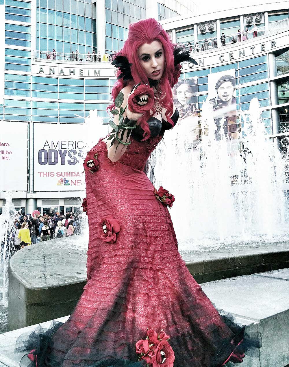 A Redd cosplayer in a long crimson gown studded with fanged
               roses, posing on the edge of the fountain outside
               the Anaheim Convention Center.