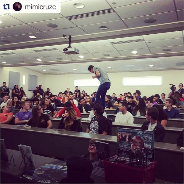 An Instagram repost by mimicruzc: Beddor standing up on a desk
               at the front of a packed lecture hall, students watching from the
               tiered rows.