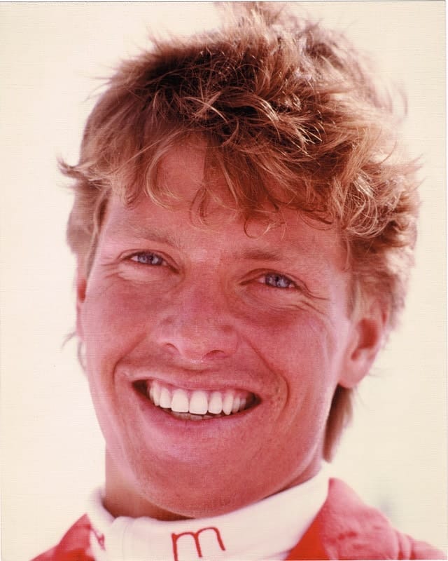 A publicity headshot from the skiing years: Beddor in his
               twenties, sunburnt and fair-haired, laughing at the camera with
               the collar of a red race suit at his neck.