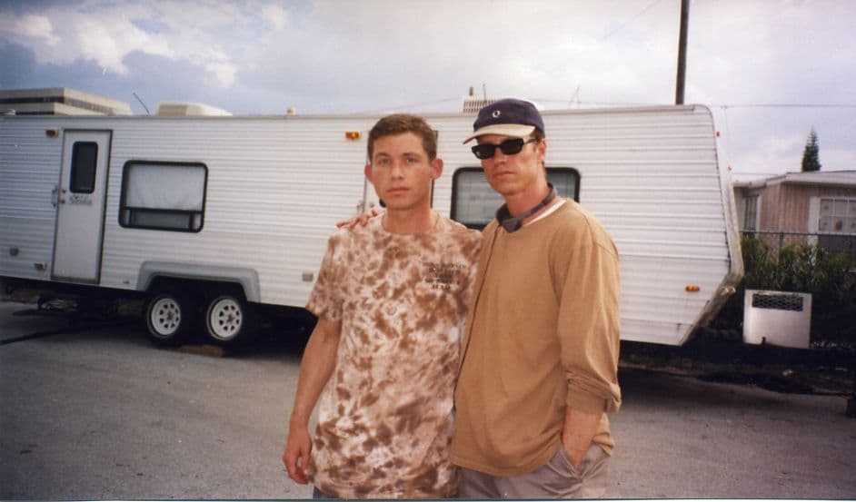 Beddor on location beside a white production trailer under a
               grey sky, in a baseball cap, sunglasses and headphones round his
               neck, one arm across the shoulders of a younger man in a
               tie-dyed T-shirt.