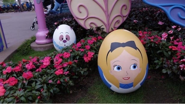 Oversized Alice and the White Rabbit as painted eggs in the Disney style displayed among pink flowers in a garden