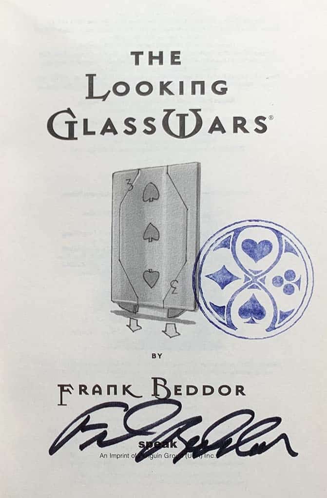 The title page signed in black ink by Frank Beddor, beside a hand-drawn card soldier and a blue Wonderland seal.