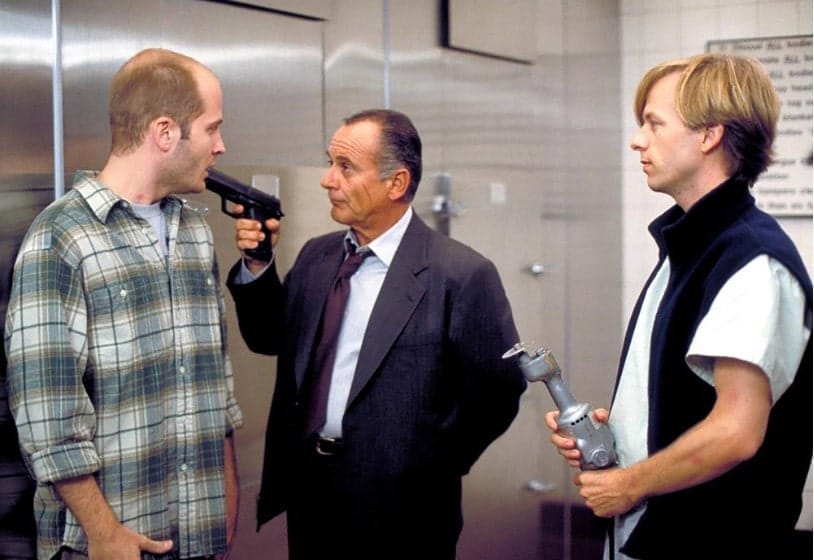 Actor, Joe Pesci holding a gun to the head of another actor, while David Spade looks on. This is a scene from the 1997 film: 8 Heads in a Duffel Bag. 
      