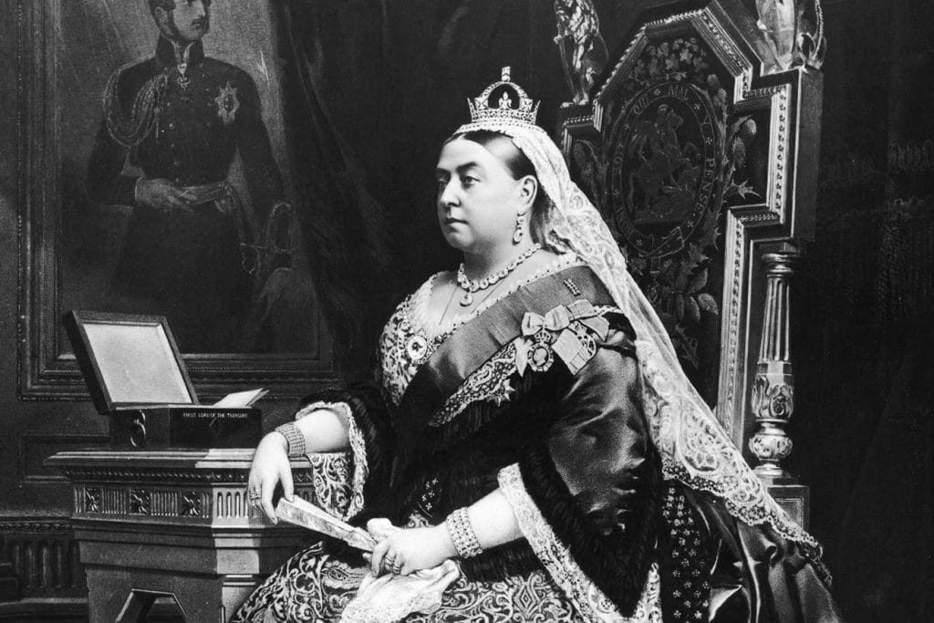 Old black &amp; white photograph of England's Queen Victoria, wearing a crown and tiara, sitting on her throne. She was a massive inspiration to Lewis Carroll's Alice's Adventures in Wonderland. 