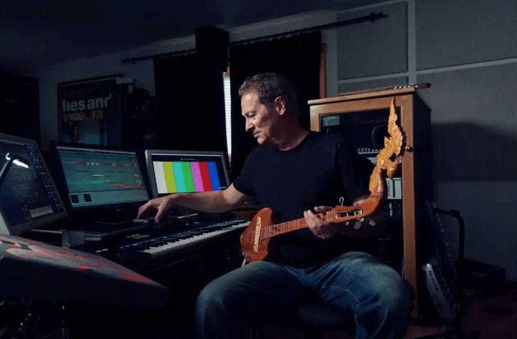 Composer Cliff Martinez working in a recording studio while holding a brown guitar. 