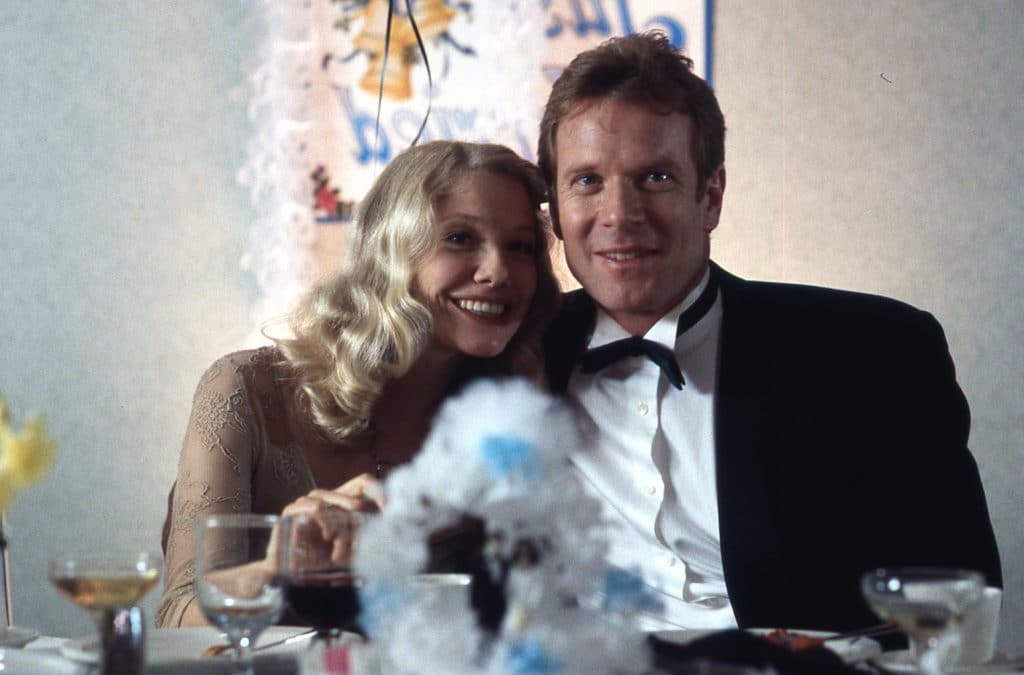 Still image from the thriller movie "Wicked" featuring William R. Moses and Louise Myrback sitting together at a wedding reception. 