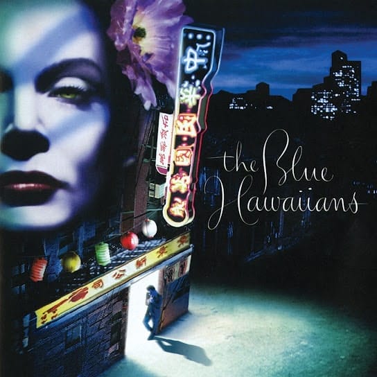 Image of The Blue Hawaiians' 1999 album, "Savage Night," featuring a woman's face superimposed on the exterior of a nightclub against the backdrop of a city. 