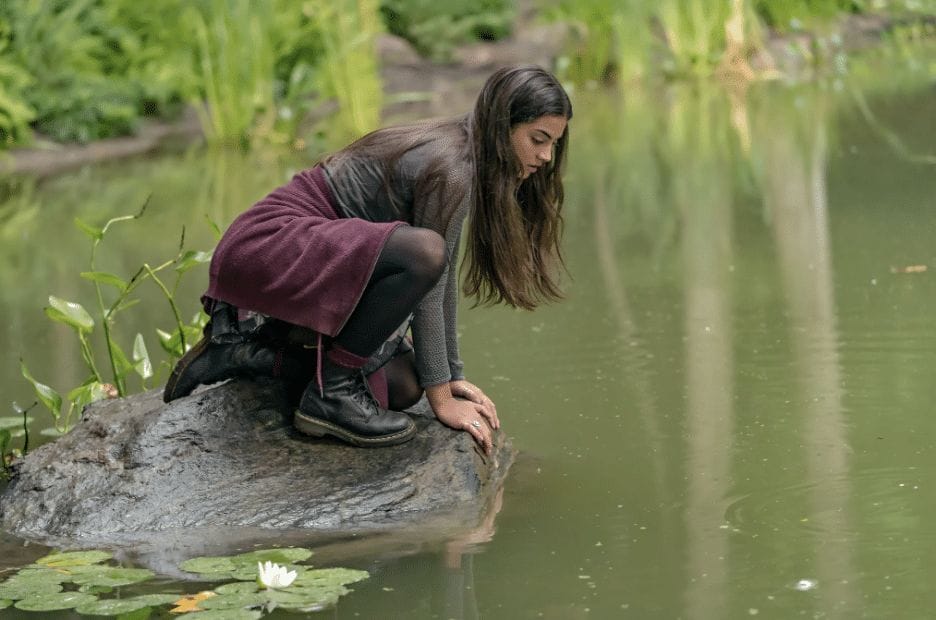 A still image from the Hallmark Channel original series "The Way Home" featuring Sadie Laflamme-Snow as Alice staring into a pond. 