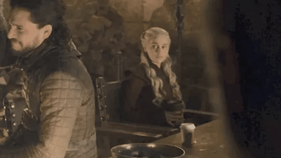 Still image from the HBO fantasy series "Game of Thrones" featuring Kit Harington as Jon Snow, Emilia Clarke as Daenerys Targaryen, and a coffee cup on a table. 
