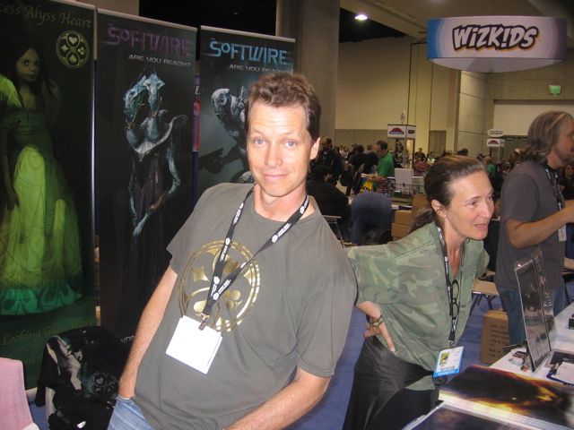 Frank Beddor and Liz Cavalier behind a convention booth,
                    a Princess Alyss Heart banner standing behind them and the
                    hall crowded in the background.