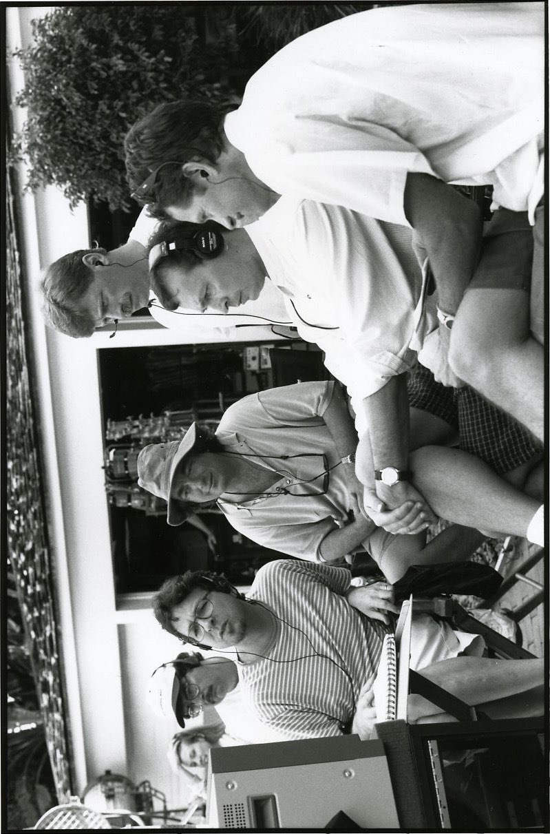A black-and-white set photograph: six of the crew crowded round
                    a monitor at the video village, most of them in headphones,
                    with Cameron Diaz waiting behind them.