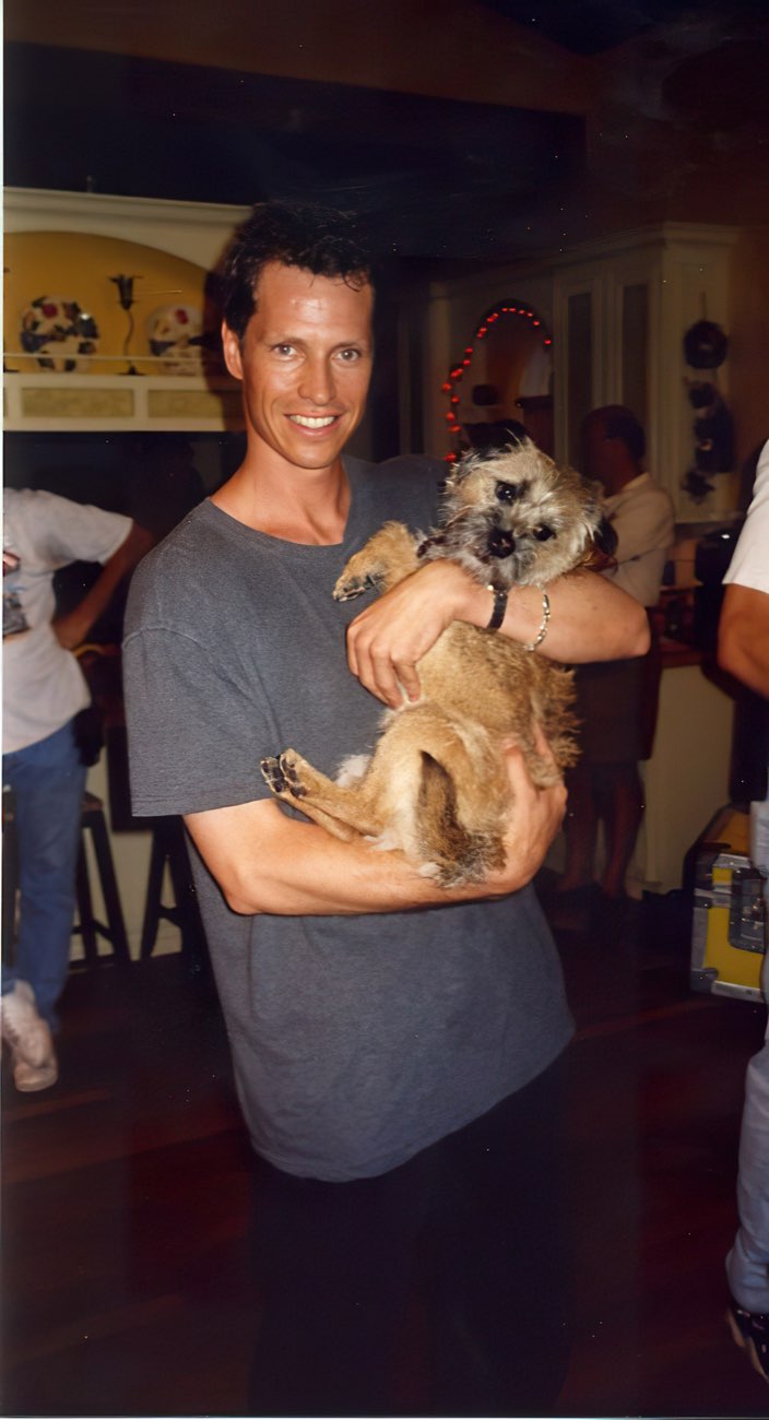 Frank Beddor on set, grinning, holding the border terrier who
                    plays Puffy in both arms like a baby.