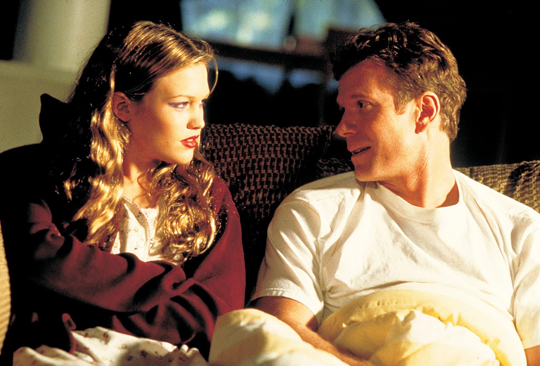 Ellie and her father Ben close together on the sofa at night,
               a quilt across both their laps, turned to look at one another
               mid-sentence. She is in her mother&rsquo;s dressing gown with
               her lipstick on.
