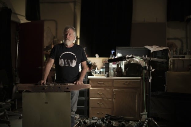 Andy Malcolm on his foley stage is well lit in a dark room with a boom mic pointing towards the stage