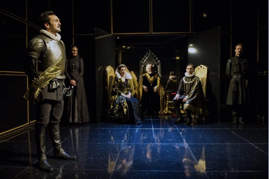 A stylistic and dark representation of Mark Bailey's set design where a king and queen preside over armored soldiers in a blackbox theater