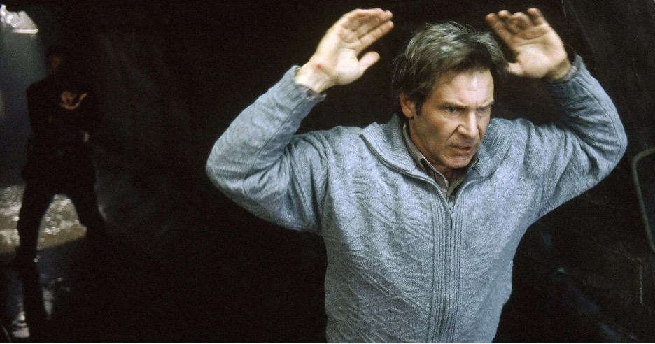 Harrison Ford, with his hands up. Tommy Lee Jones is behind him, holding a gun. A scene from the movie The Fugitive. 