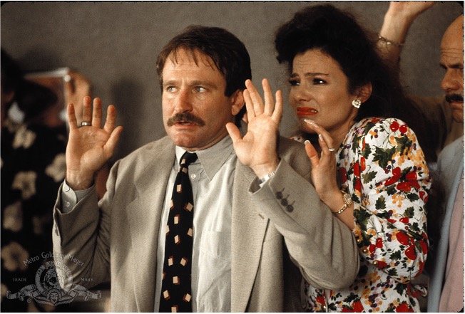 Robin Williams with a mustache, holding his hands up. From the Movie Cadillac Man, Fran Drescher is standing behind him, also with her hands up, looking scared.  