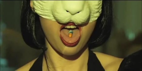 A person with a pill in her mouth, wearing a rabbit mask, reminiscent of Lewis Carroll's Alice's Adventures in Wonderland. From the music video for the Natalia Kills song: "Wonderland". 