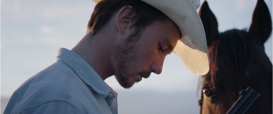 Image of a cowboy, wearing a cowboy hat, standing next to a pretty horse. Intent of image is to show some beautiful cinematography in The Rider, by Choe Zhao. 