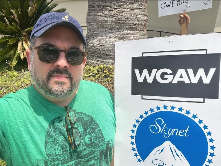 Image of Chris Monfette, holding a picket sign as he is participating in the WGAW strike. The Writer's Actors Guild of America West strike in Hollywood. Which focuses on AI so he wrote Skynet in the Paramount logo for his sign. 