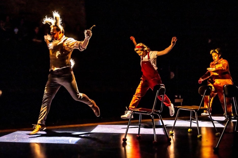 Image of 3 actors from Bad Hats Theatre group, performing Alice in Wonderland. They are jumping on the stage with the White Rabbit leading two others in a song and dance number. 