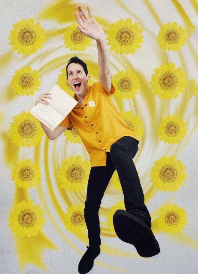 Booktuber, Jessethereader jumping with his hand up, holding an open book. He's wearing a yellow shirt and black pants. He's in a background with yellow sunflowers, swirled around. 
