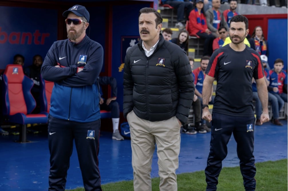 Image of the coaching staff from the Apple TV+ series: Ted Lasso. With characters left to right: Coach Beard, (Brendan Hunt), Ted Lasso (Jason Sudeikis) and Roy Kent (Brett Goldstein). 