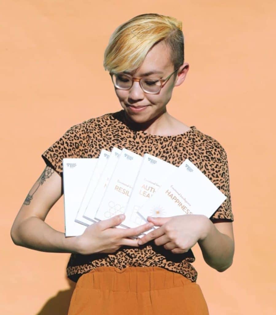 Image of Withcindy, a YouTube content creator.  holding several books in a series. She is wearing glasses, a leopard print shirt and orange pants. 