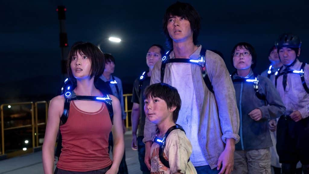 Kento Yamazaki, Tao Tsuchiya, and other actors wearing glowing harnesses in a still from the Netflix science fiction series "Alice in Borderland." 