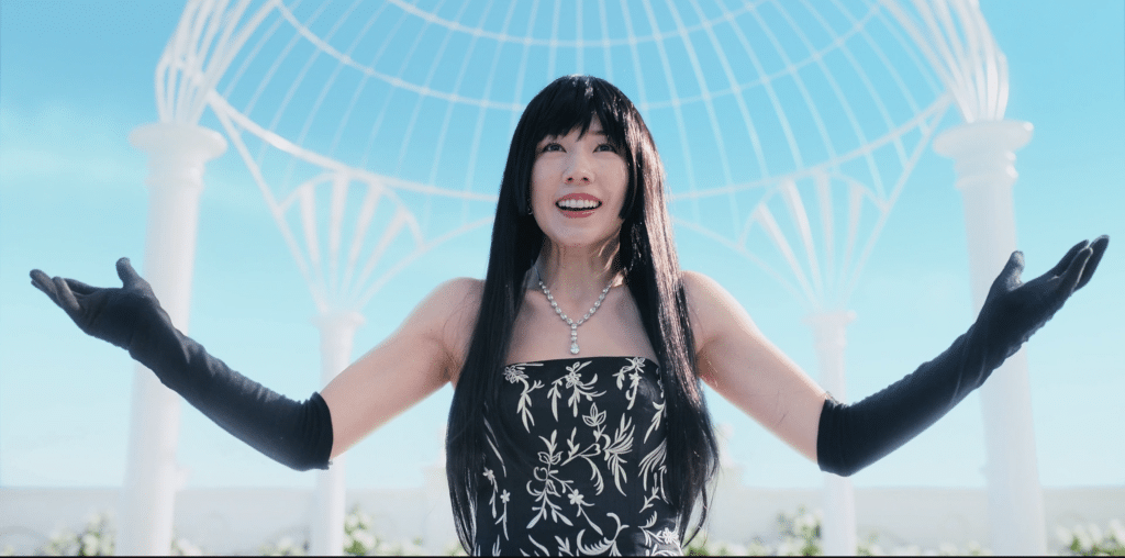 Riisa Naka, wearing a black and white dress and black gloves, smiles and raises her hands in a still from the Netflix science fiction series "Alice in Borderland." 