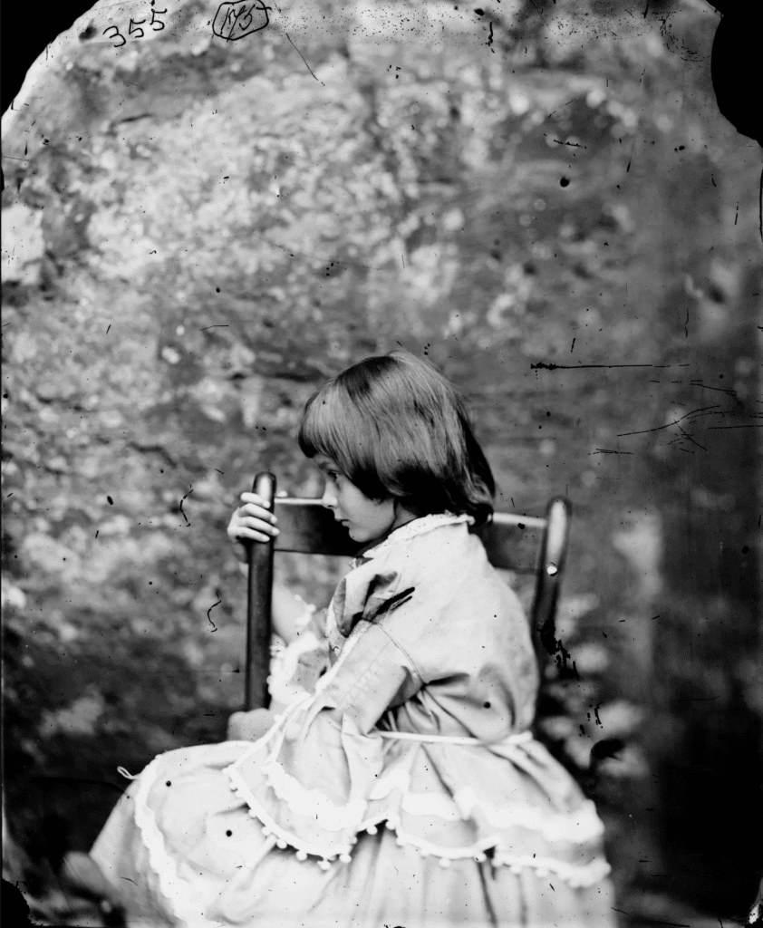 Photograph of Alice Liddell wearing a dress and sitting sideways in a chair taken by Lewis Carroll in 1858. 