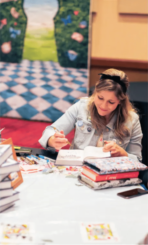 Author Sara Ella signing books at a table.