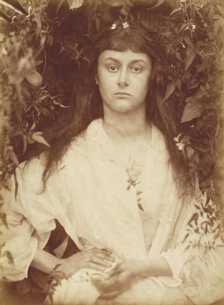 Photograph of Alice Liddell, wearing a white dress and surrounded by foliage, taken by Julia Margaret Cameron in 1872.