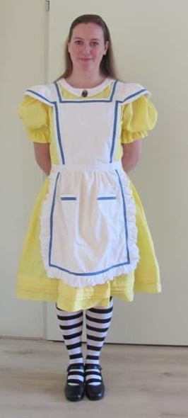 Image of Lenny de Rooy in a yellow dress, blue and white apron, black and white striped socks, and black shoes. 