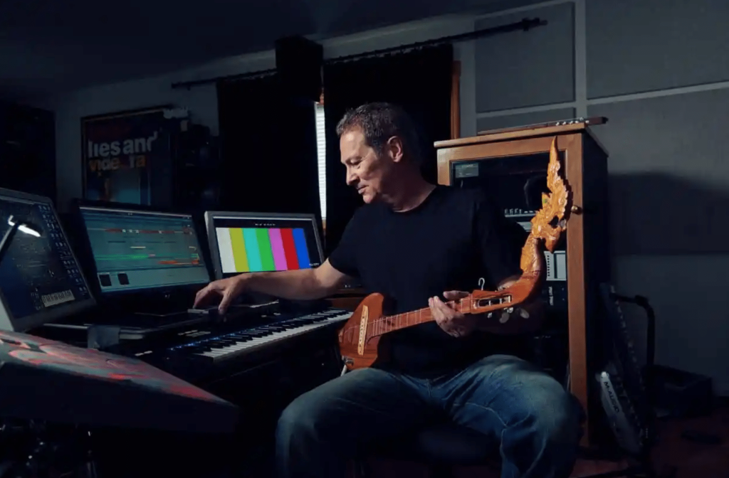 Composer Cliff Martinez working in a recording studio while holding a brown guitar. 