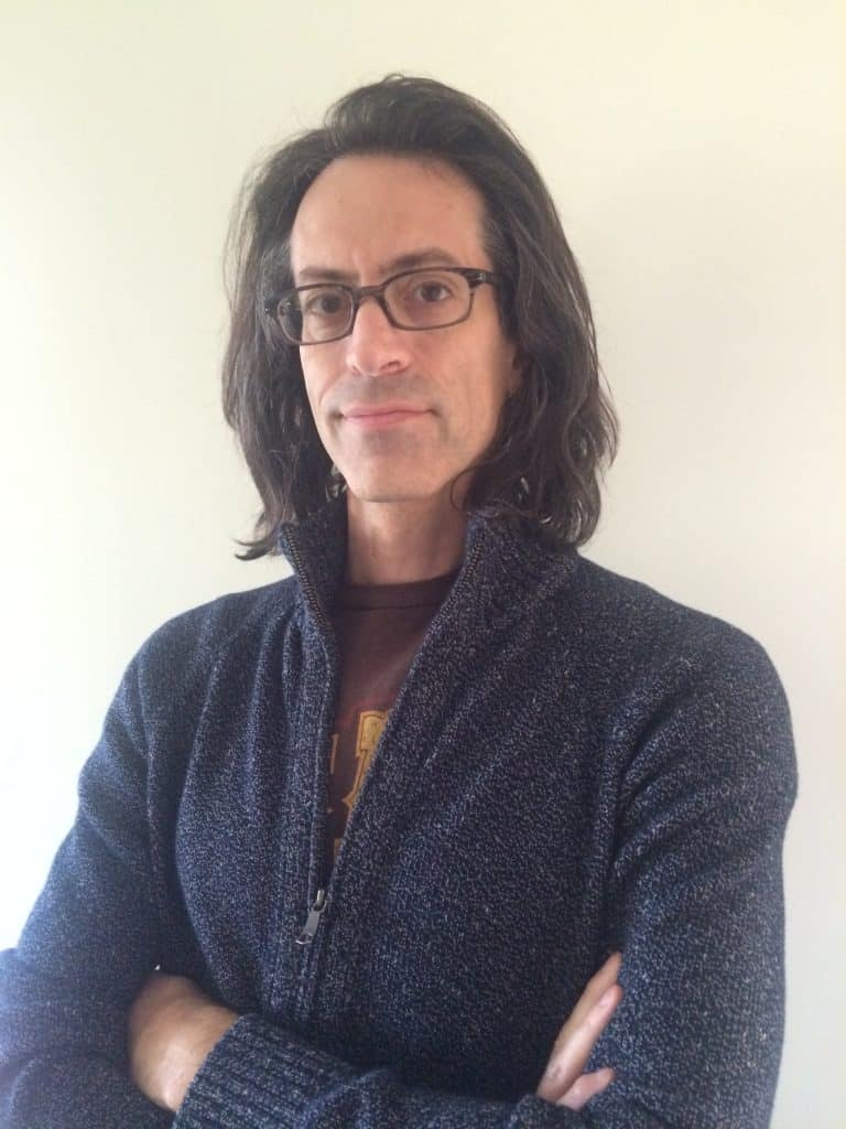 Eric Laster, author of the coming-of-age supernatural mystery novel "Static," posing with folded arms in a blue sweater. 