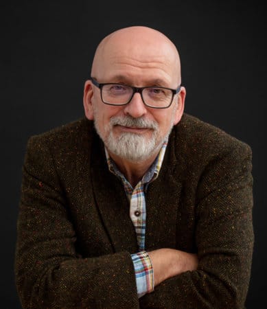 Photograph of Booker Prize-winning Irish author Roddy Doyle wearing a brown blazer and checked button-down shirt. 