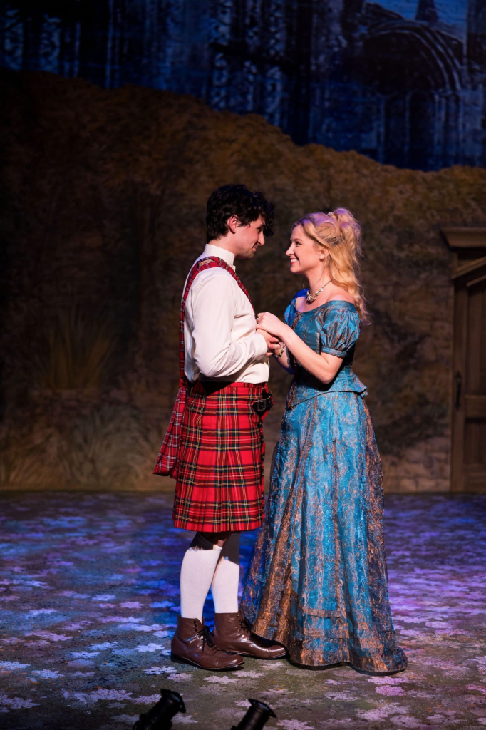 A still image featuring Alice Liddell in a blue dress and Prince Leopold in a kilt from the production of the musical "Alice, Formerly of Wonderland".