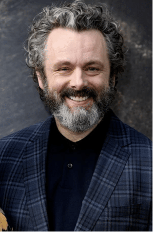 Photograph of actor Michael Sheen in a dark blue checked blazer and solid navy blue button-down shirt. 