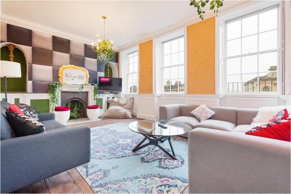 Living room featuring yellow, green, and black-and-white checked wallpaper and a "Have I Gone Mad?" sign above the fireplace from The Wonderland Townhouse in Bath, England. 