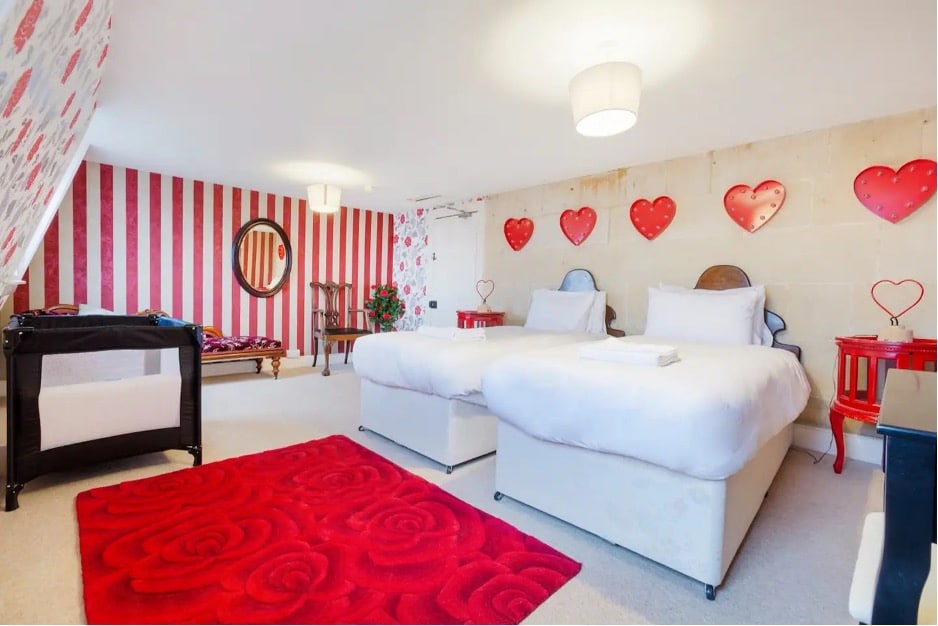 Bedroom with a red rose-themed rug, red and white striped wallpaper, and heart decorations from The Wonderland Townhouse in Bath, England. 