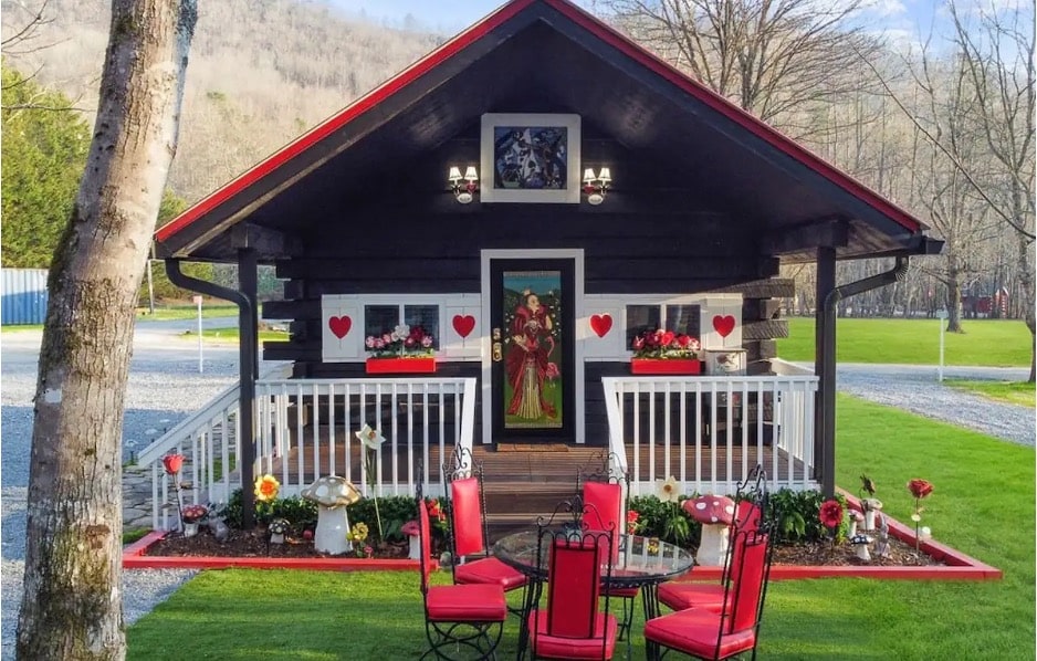 The front of a small, black house with red trim and Queen of Hearts decorations from the Alice's Queen Cottage Airbnb in Hayesville, North Carolina. 