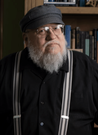 Photograph of "Game of Thrones" author George R.R. Martin wearing glasses, suspenders, and a gray cap. 