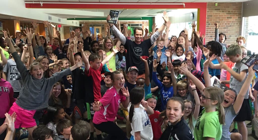 Photograph of author Frank Beddor and a crowd of elementary school children cheering at an even for his middle-grade fantasy novel "Hatter Madigan: Ghost in the H.A.T.B.O.X."