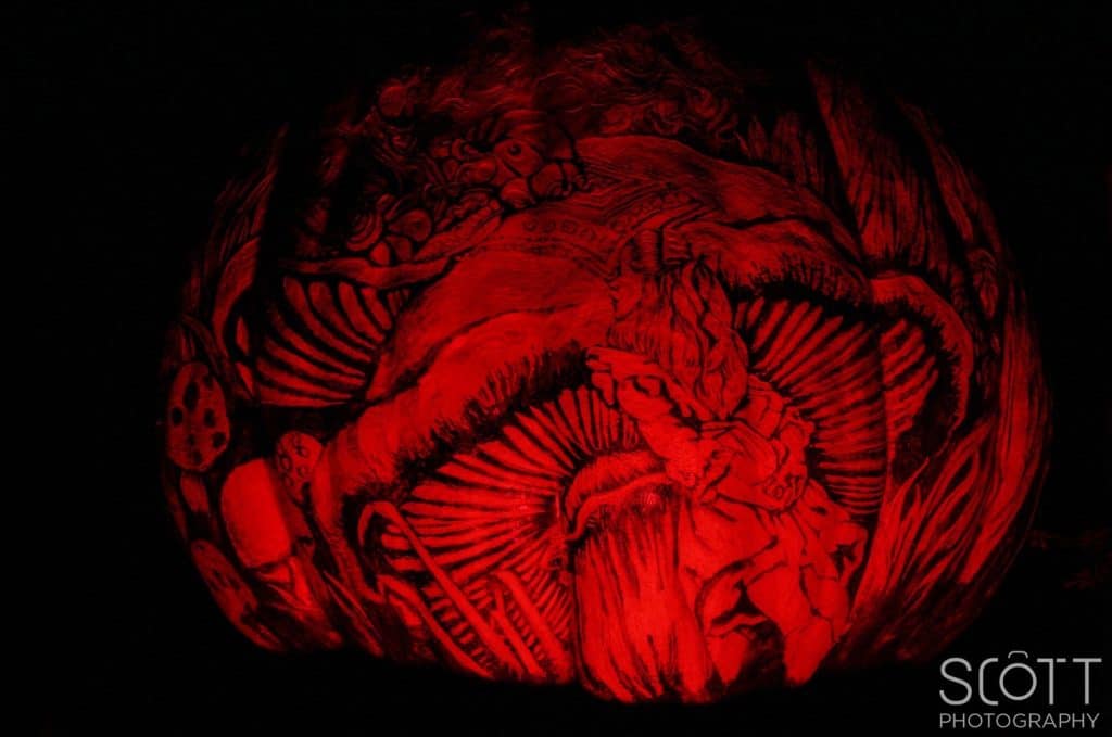 A photograph of a pumpkin carved to depict a Alice speaking to the Caterpillar from "Alice in Wonderland".