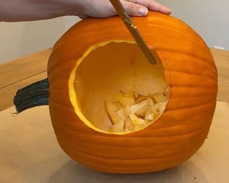 A photograph of a pumpkin with a circular hole carved into it. 