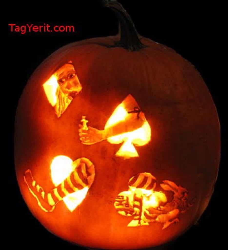 A photograph of a pumpkin carved with the four playing card suits with Alice from "Alice in Wonderland" behind the suits. 