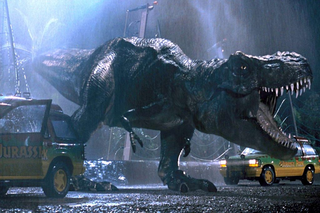 A screenshot from Steven Spielberg's 1993 film "Jurassic Park," featuring a Tyrannosaurus Rex roaring in the rain. 